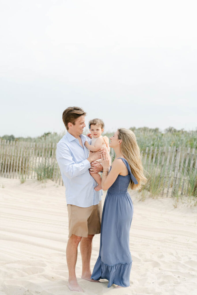 Young couple poses with baby by the sand dunes at the Bethany Beach Delaware.