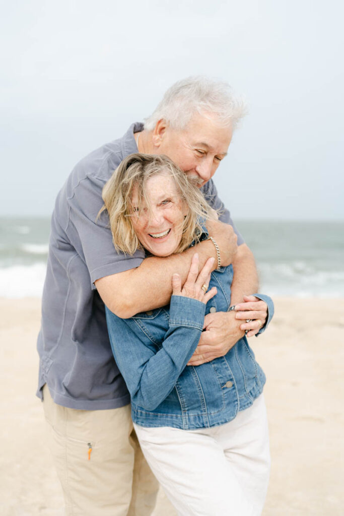 Older couple hugs on Bethany beach in Delaware. 
