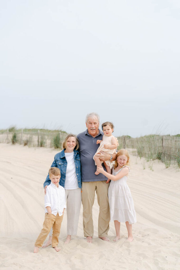Grandparents pose with young grandchildren in the sand dunes at bethany beach.
