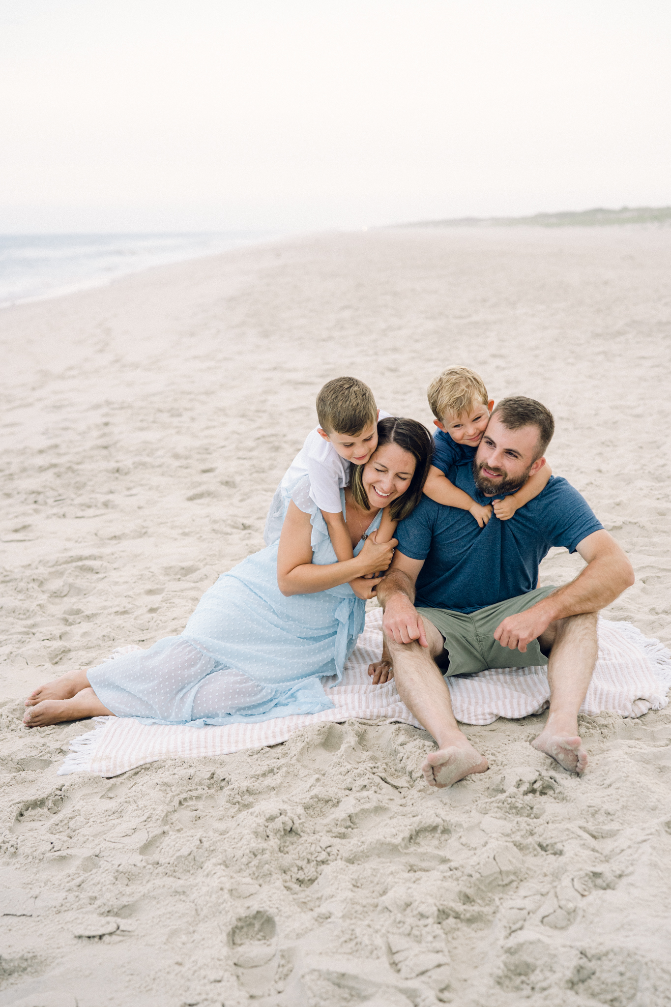 Family of four cuddles on the beach during photo session with Bethany Beach family photographer