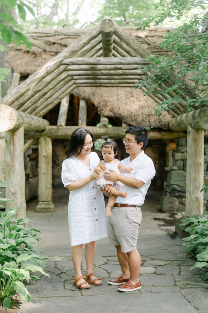 couple in white linen poses with their baby near the children's garden at the Winterthur Estate.