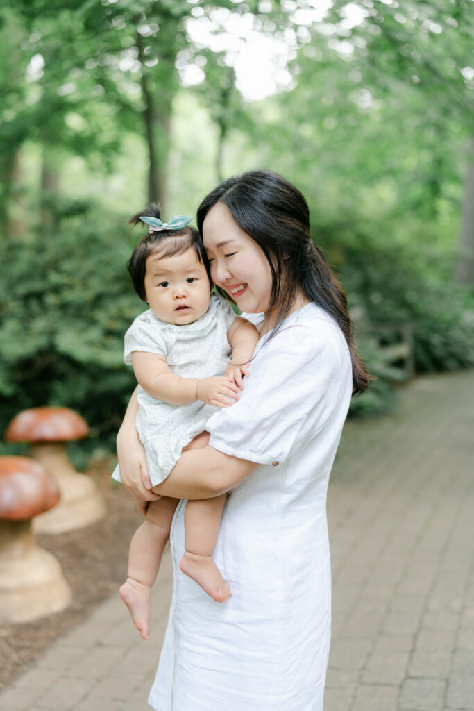 Dark-haired mother holds baby girl in dress in Wilmington DE garden