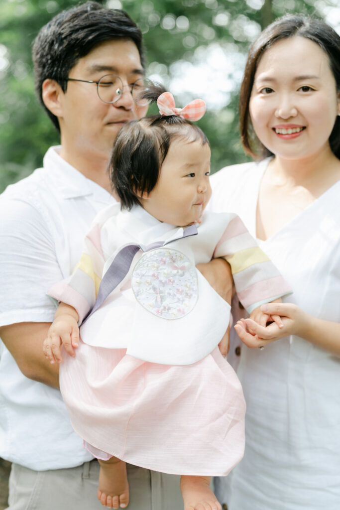 Toddler dressed in traditional korean gown poses with parents in Winterthur gardens 