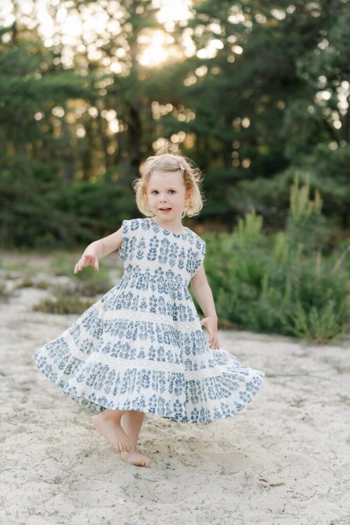 Little blonde haired girl twirls in dress in the sand