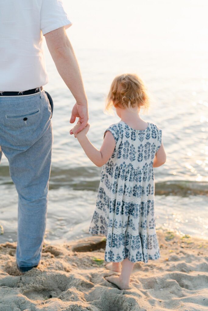 father holds daughter's hand at the ocean 