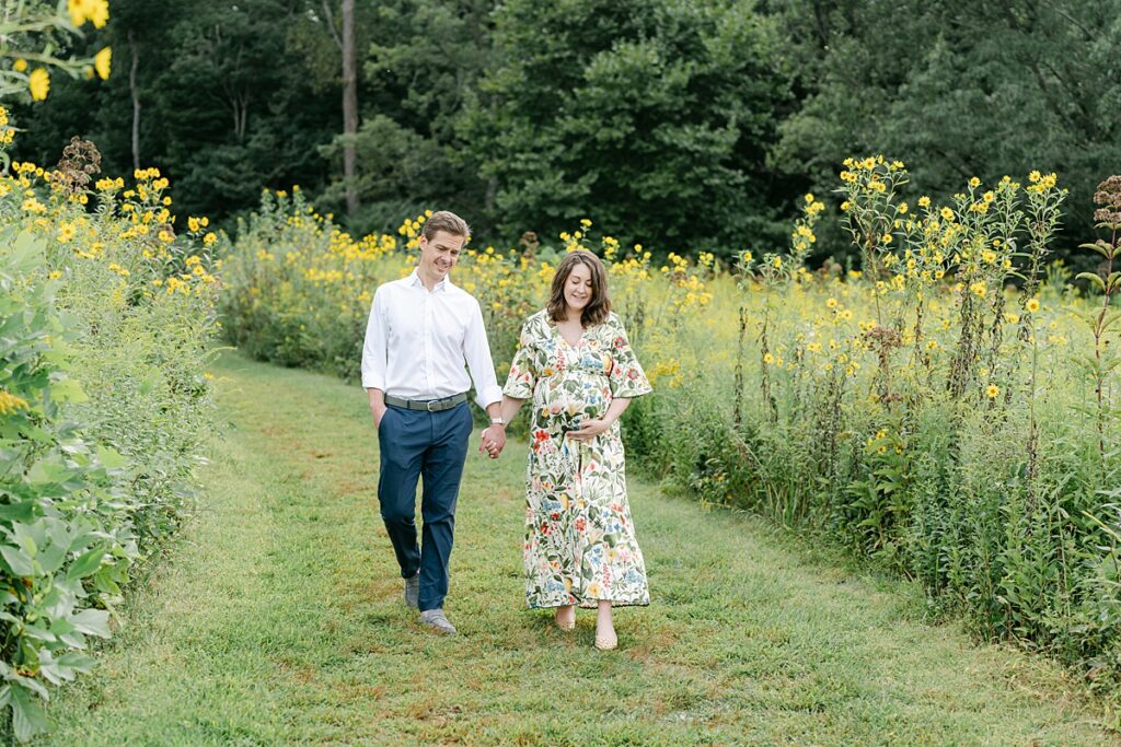 a maternity session for pregnant mom and husband holding hands walking through wildflowers at Longwood Gardens