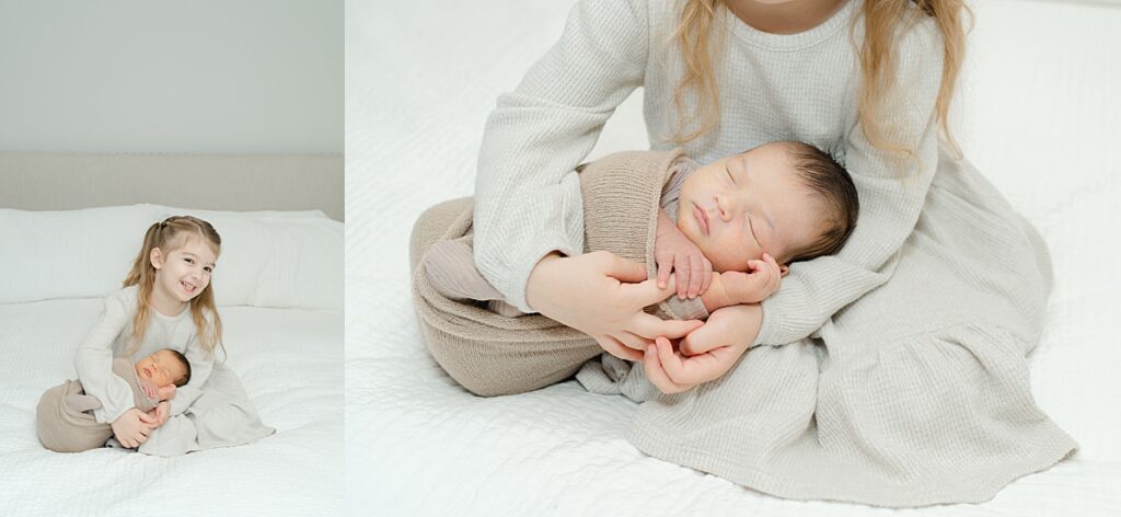 big sister holding newborn baby brother on bed in neutral clothing during a Philadelphia in-home newborn photography session