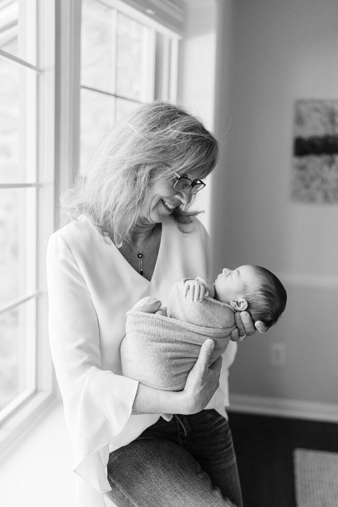 grandmother sitting in bay window holding newborn boy during a Philadelphia in-home newborn photography session