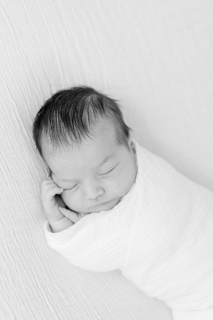 black and white image of newborn boy swaddled and sleeping