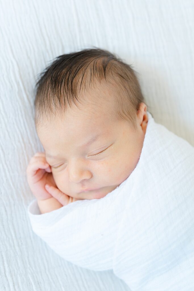 newborn baby sleeping while swaddled in white blanket