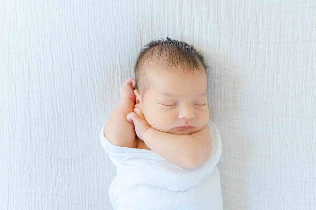Using natural window light, AnneMarie Hamant is an expert Philadelphia In-Home Newborn Photographer, posing baby boy sleeping in a white swaddle