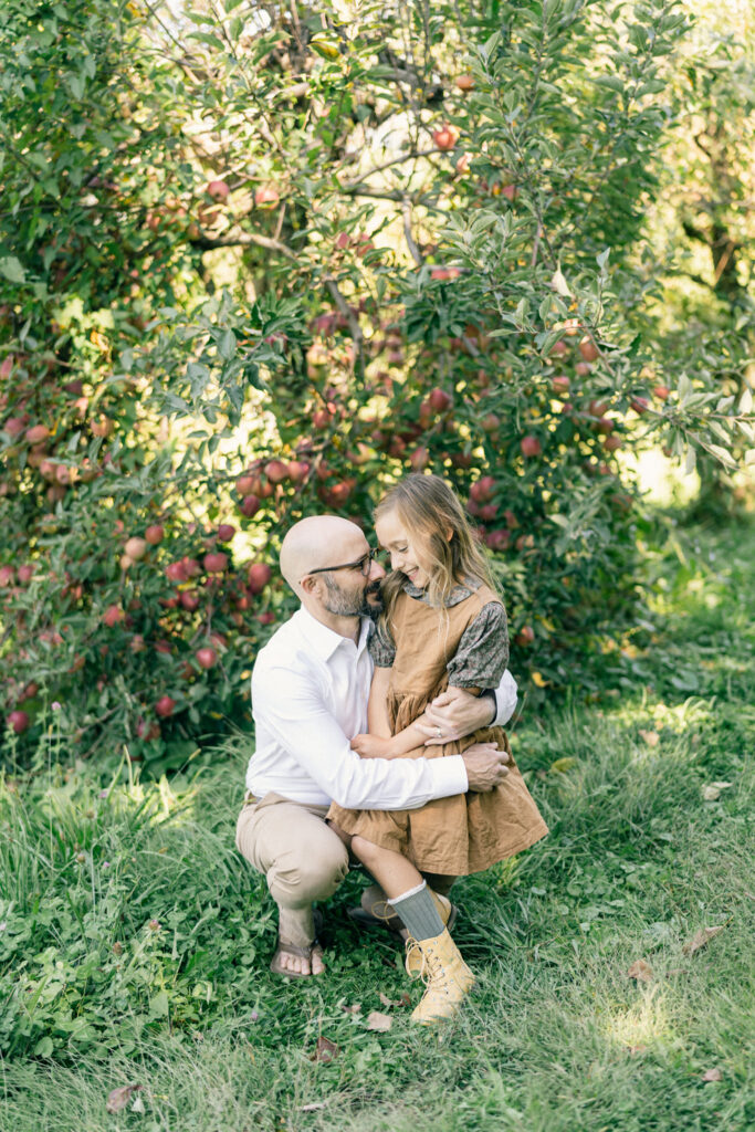 Father and daughter embrace in front of an apple tree in an orchard in Kennett Square, PA