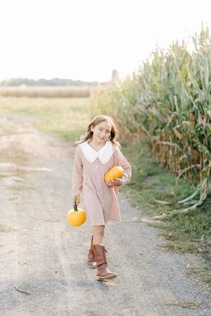 Little girl in mauve dress walks along a dirt road and cornfields at an Amish pumpkin patch near West Chester PA