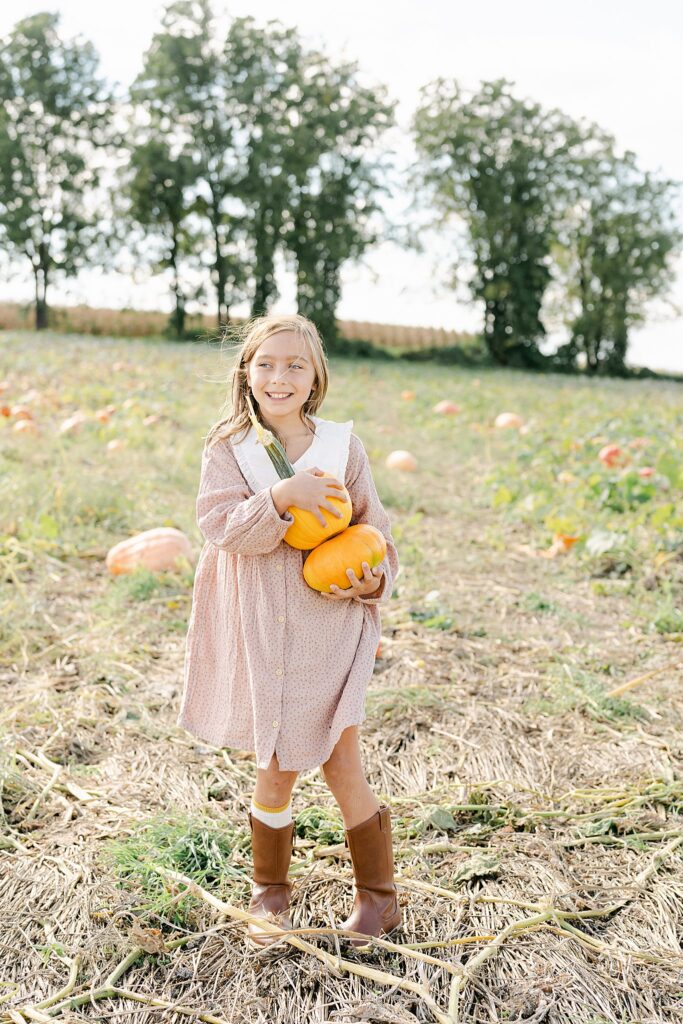 Little girl happily picks a variety of pumpkins in a pumpkin patch near West Chester PA