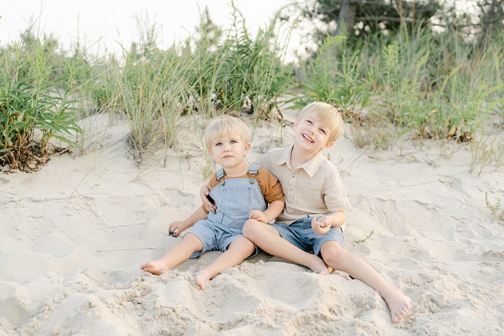 Two young boys sitting in the sand with their arms around each other at Rehoboth Beach