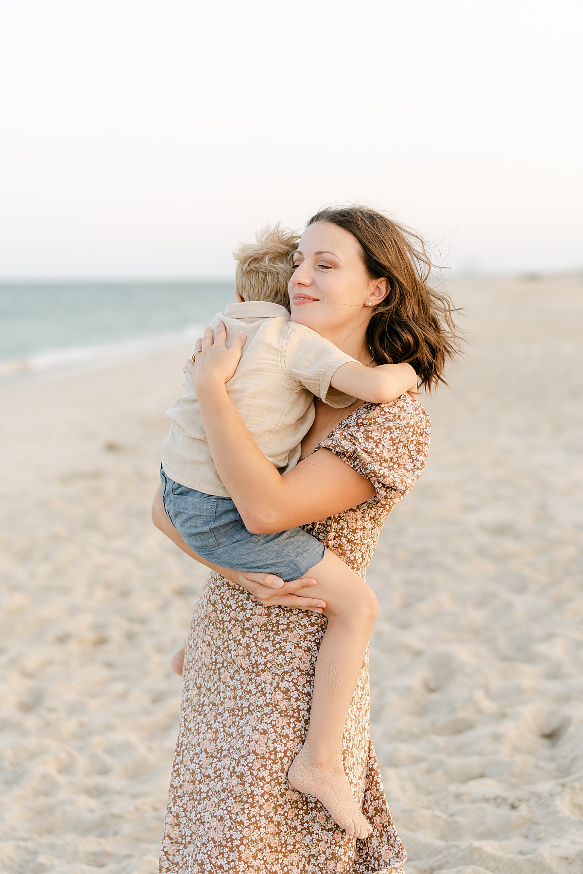 Mother embraces her toddler boy during a candid moment on Rehoboth beach with family photographer AnneMarie Hamant
