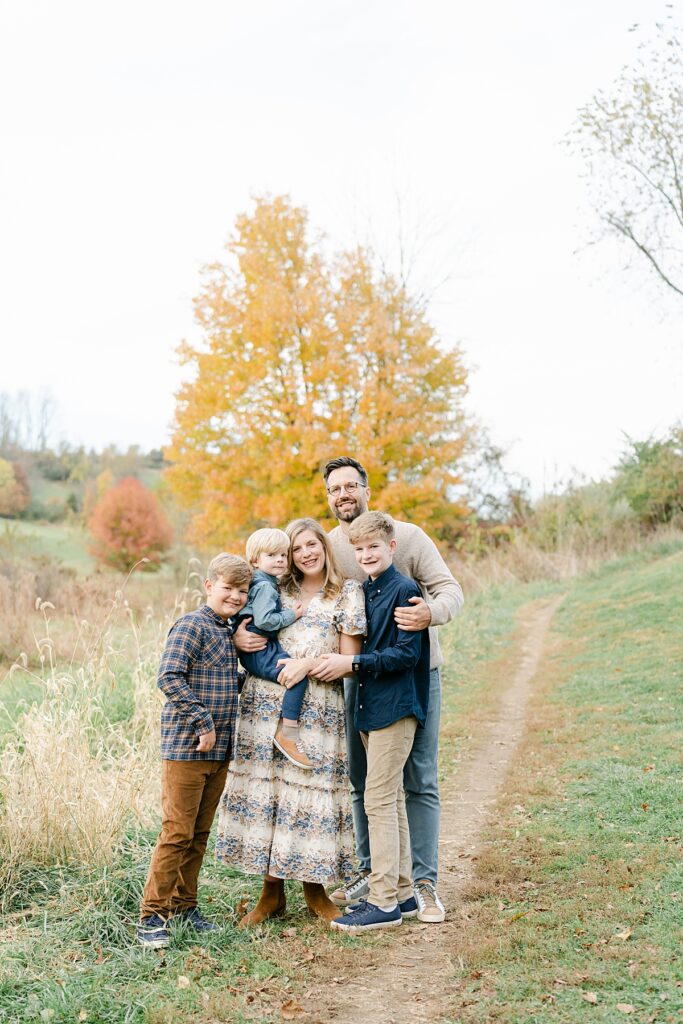 A family of five standing close together in front of fall foliage by philadelphia portrait photographer, annemarie hamant