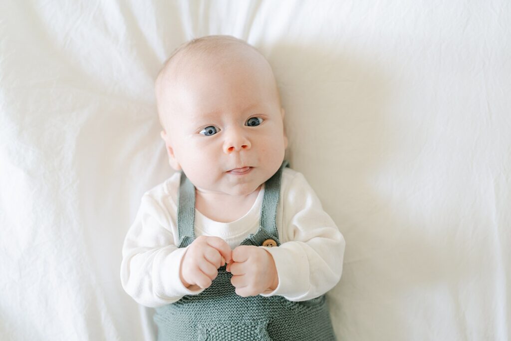 Close up of newborn 8 week old boy in a green knitted romper on a white blanket by Philadelphia Baby Photographer, AnneMarie Hamant