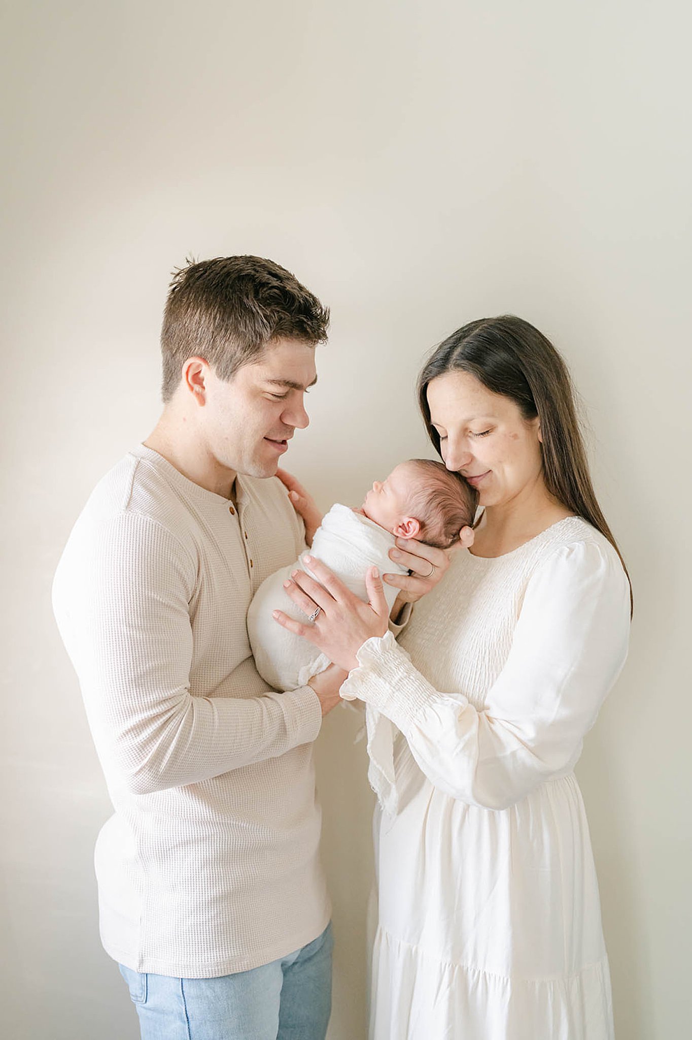 Parents hold their newborn son dressed all in white in a studio Philadelphia doulas