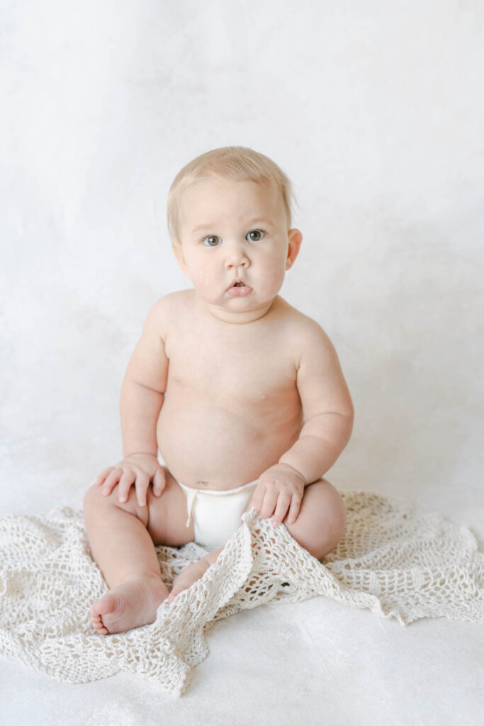baby girl sitting in diaper on a light backdrop in a Philadelphia baby photographer's studio