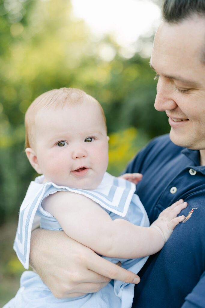 Dad in blue polo shirt holds Baby girl in classic blue and white romper with red hair