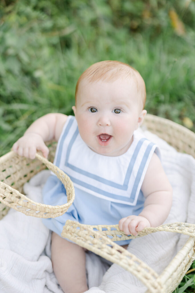 Baby girl in white and blue classic romper sits in a basket outside
