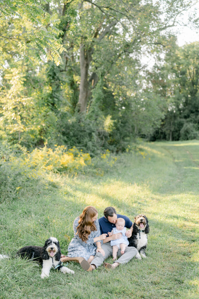 family with bernedoodles sits in the grass at sunset outside of Philadelphia PA