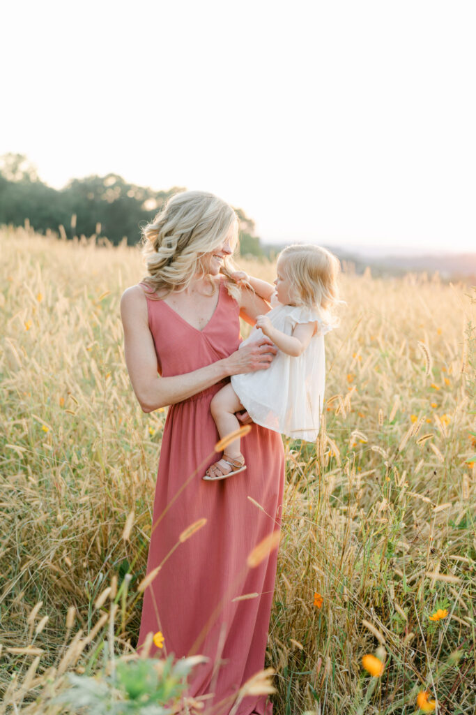 mom holds daughter in a golden field at sunset outside of Philadelphia PA