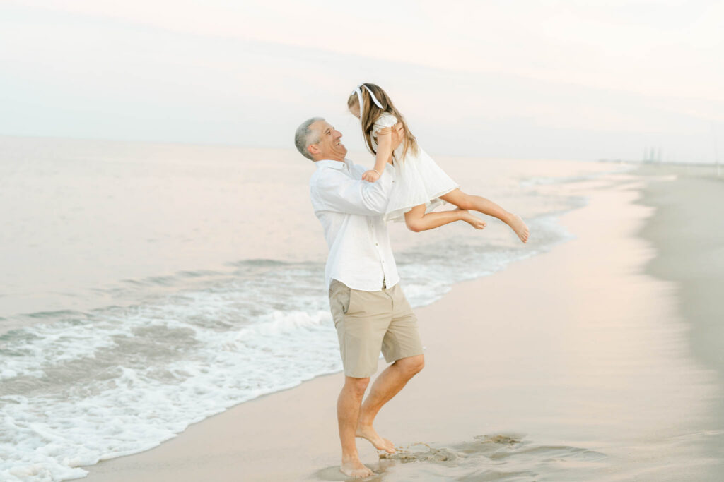 Dad lifts daughter on the beach at sunset